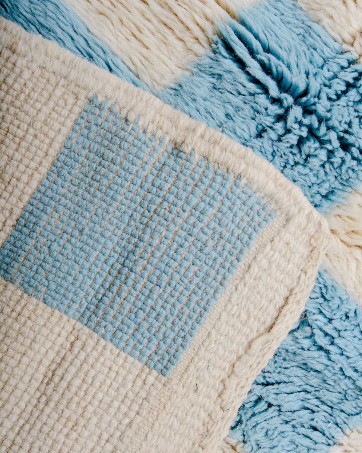 Back corner of Beni M'rirt wool rug in cream and light blue checkerboard design.